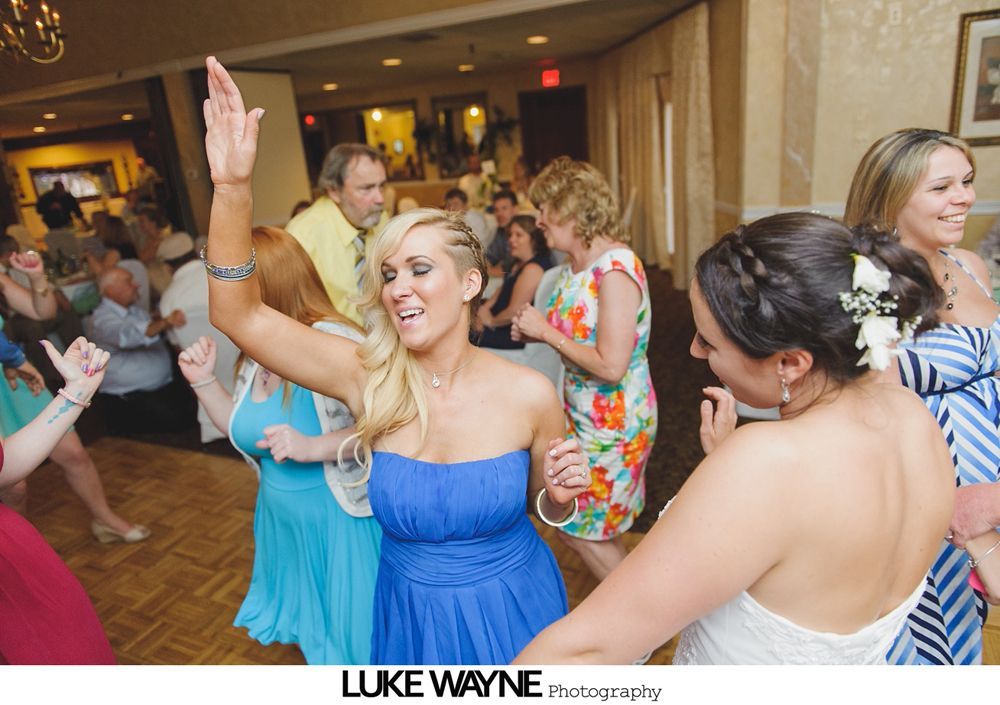 Wedding reception: guests dancing, woman in blue dress with arm raised, others smiling.