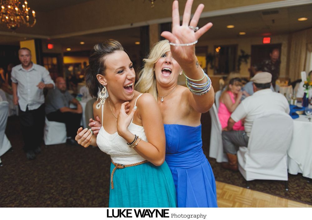 Two women dancing at an event, one in a blue dress, the other in a turquoise skirt. Both are smiling.