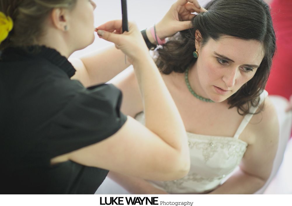 Wedding day preparation: bride in veil, another in a dress looking at her, and a bridesmaid in pink holding a card and purse.