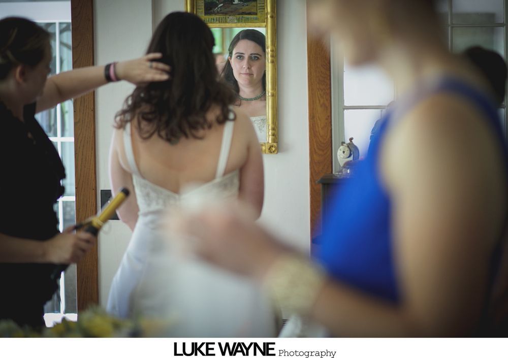 Bridesmaids in pastel dresses hold bouquets, posing outside a building next to a sign for the Hill-Stead Museum.