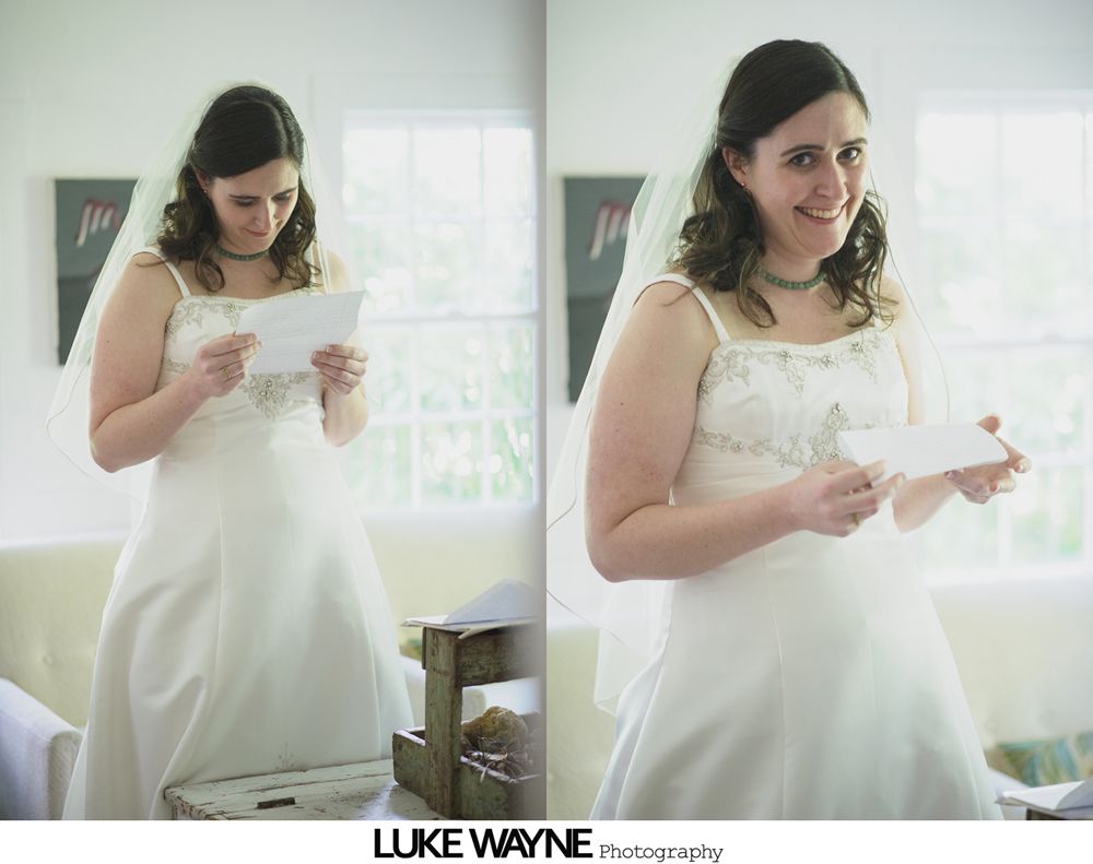 Bride in a white lace wedding dress holding a bouquet. She's outdoors on a pathway, smiling.