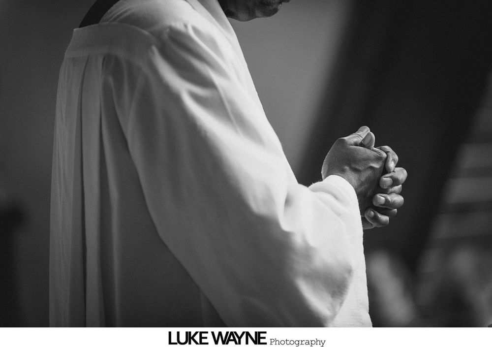 Wedding party posing in a field. People in formal wear with bouquets, smiling. Green field, cloudy sky.