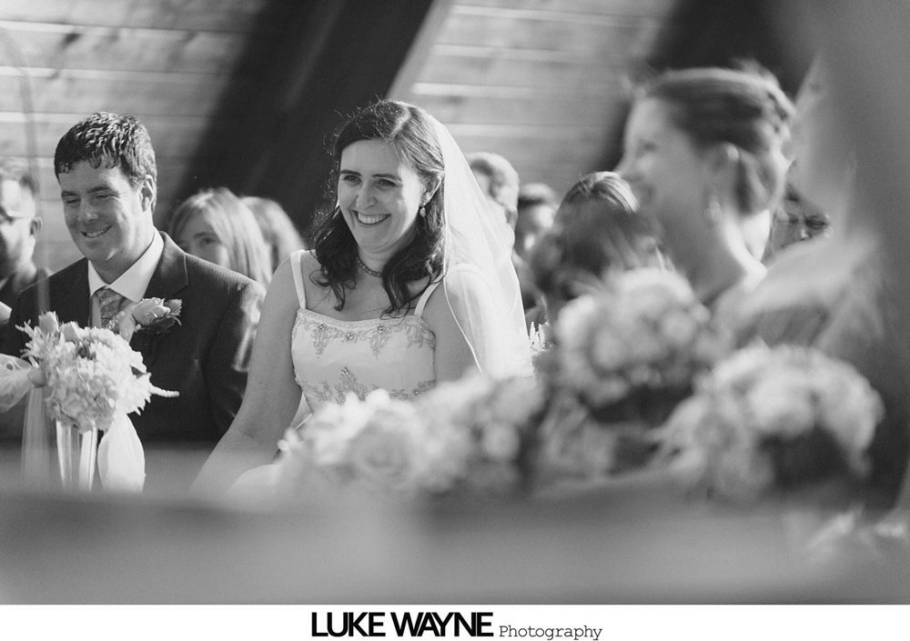 Bride and groom on a road. Man hugs woman, smiles, and holds flowers.