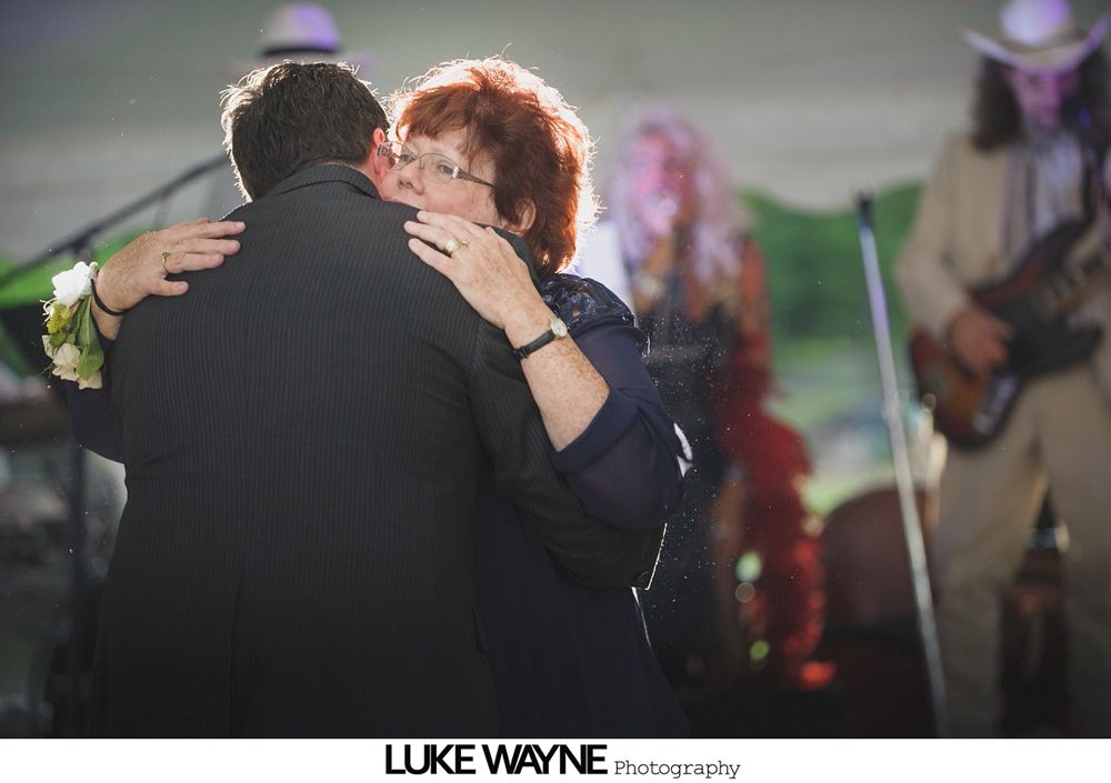 Group photo at a wedding reception. Bride and groom centered, surrounded by guests in formal attire.