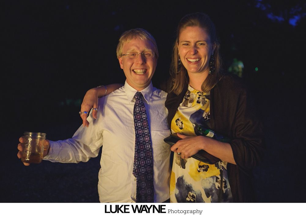 Group photo at a wedding reception. Bride and groom centered, surrounded by guests in formal attire.