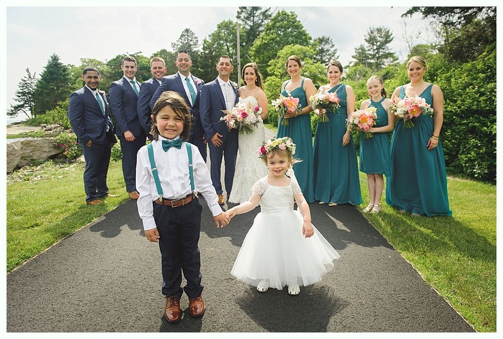 Bride in white dress holding bouquet, posing near red building; bridesmaids in navy dresses.