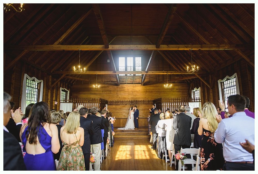Wedding ceremony in a barn; couple kissing under an archway, surrounded by guests.