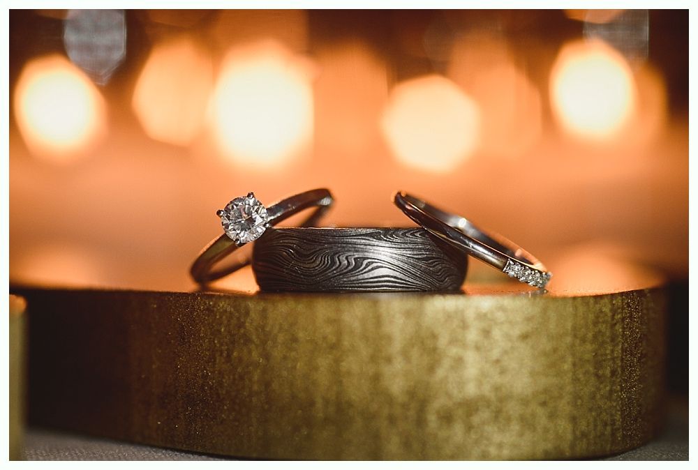 Man dances with a woman in a black dress at a wedding reception. They smile; lights and decorations in background.