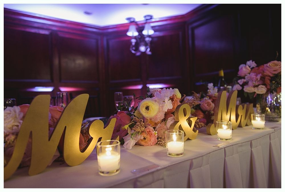Bride dancing at wedding, wearing white dress with gold belt, smiling, with groom, and guests.