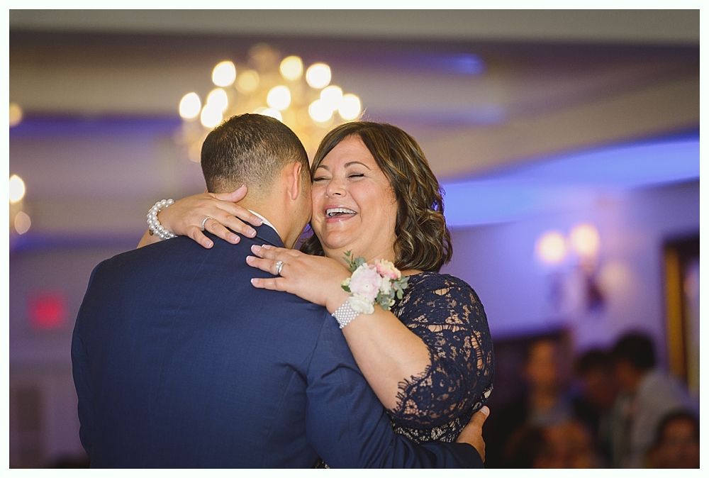Man in formal wear doing a handstand on a wooden dance floor, guests watching.