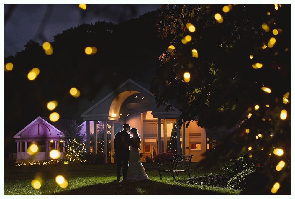 Couple kissing on steps of red building at dusk; backlit, dramatic lighting.