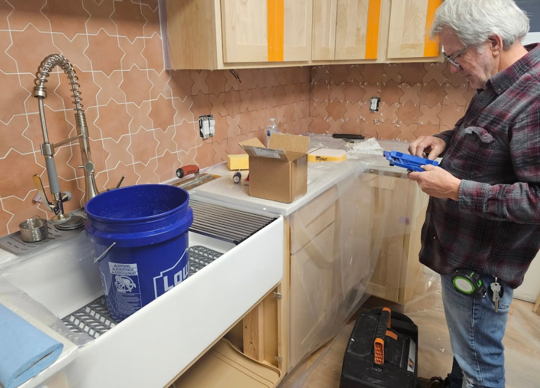 A man is working in a kitchen with a blue bucket in front of a sink.