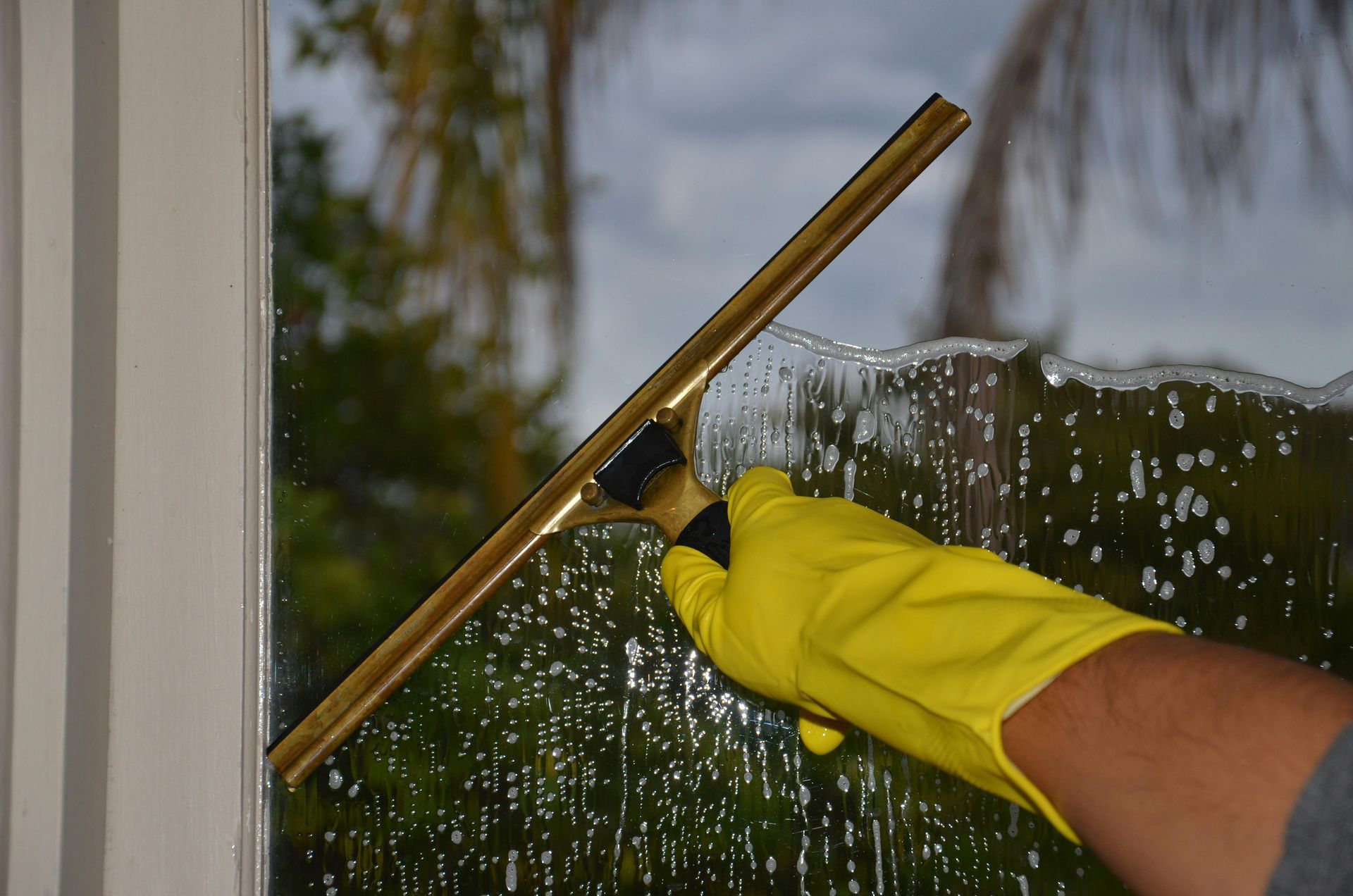 Yellow-gloved hand using a squeegee to clean a rain-speckled window