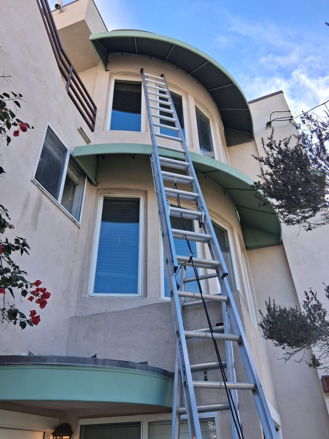 Ladder leaning against a multi-story building with windows and green awning.