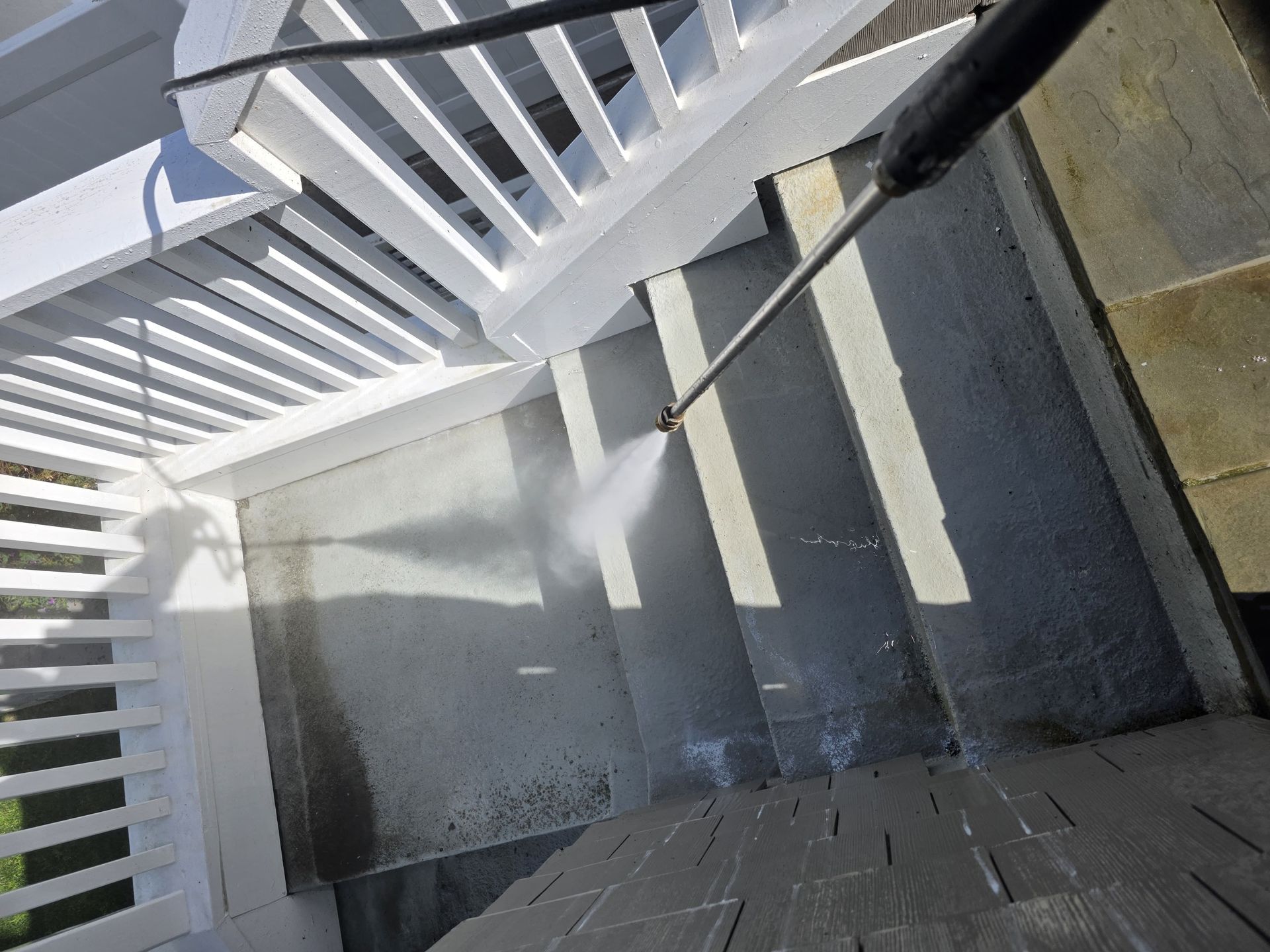 Power washer cleaning stone steps under a white pergola.