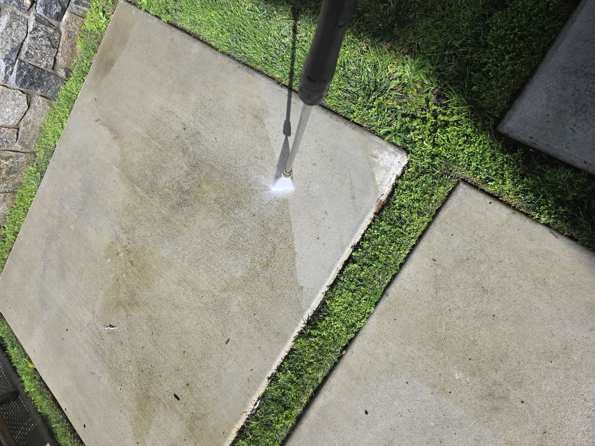 Person power washing a cedar shingle roof. Water sprays across the brown shingles on a sunny day.