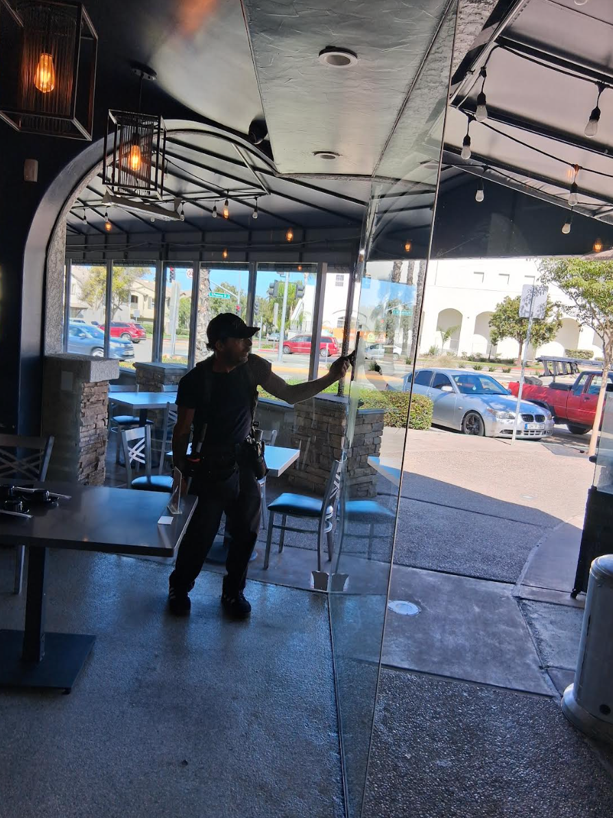 Person inside a restaurant doorway, holding a cleaning implement, view of street and parked cars.