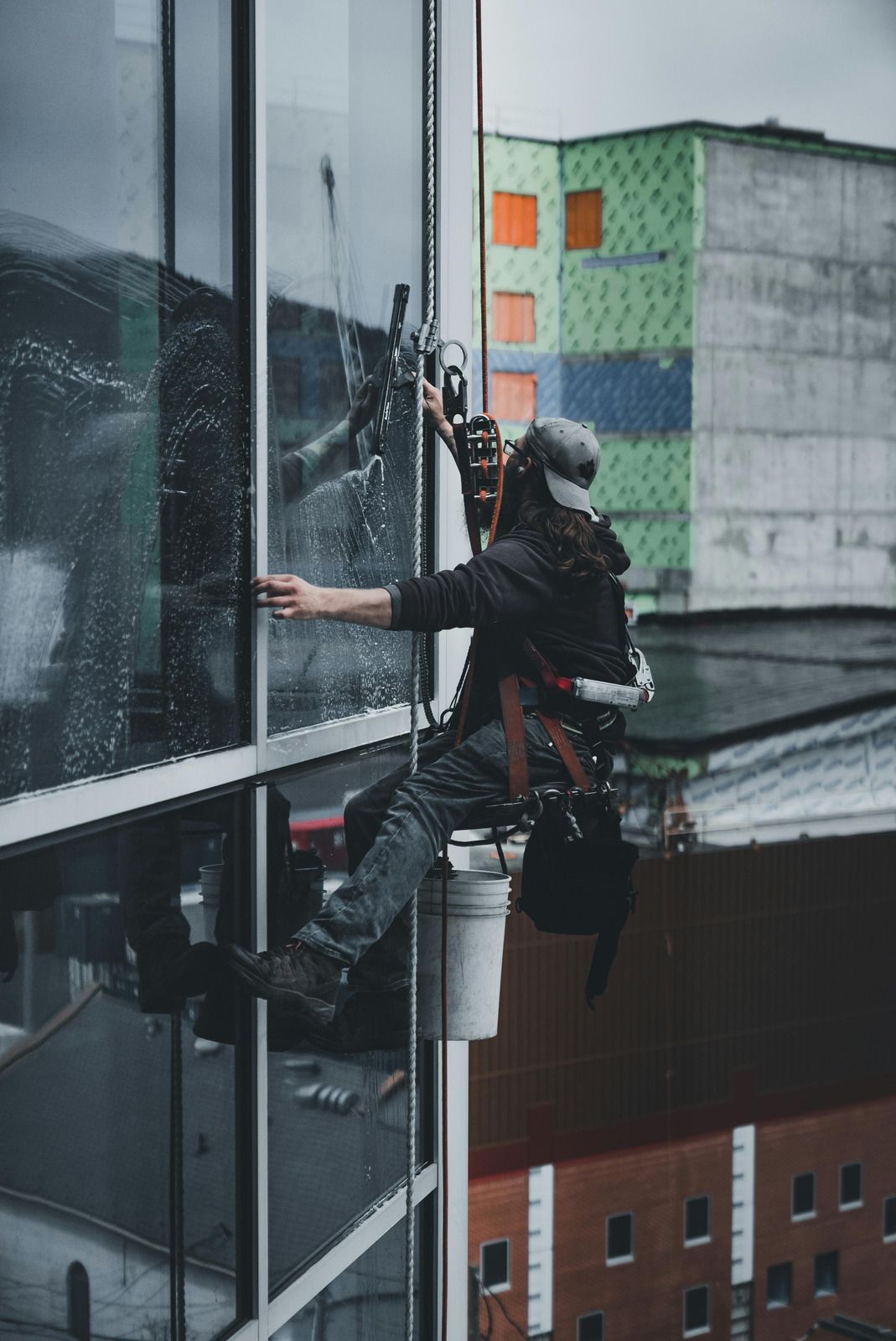 Window washer suspended on a high-rise building, cleaning a glass panel. The worker wears safety gear.