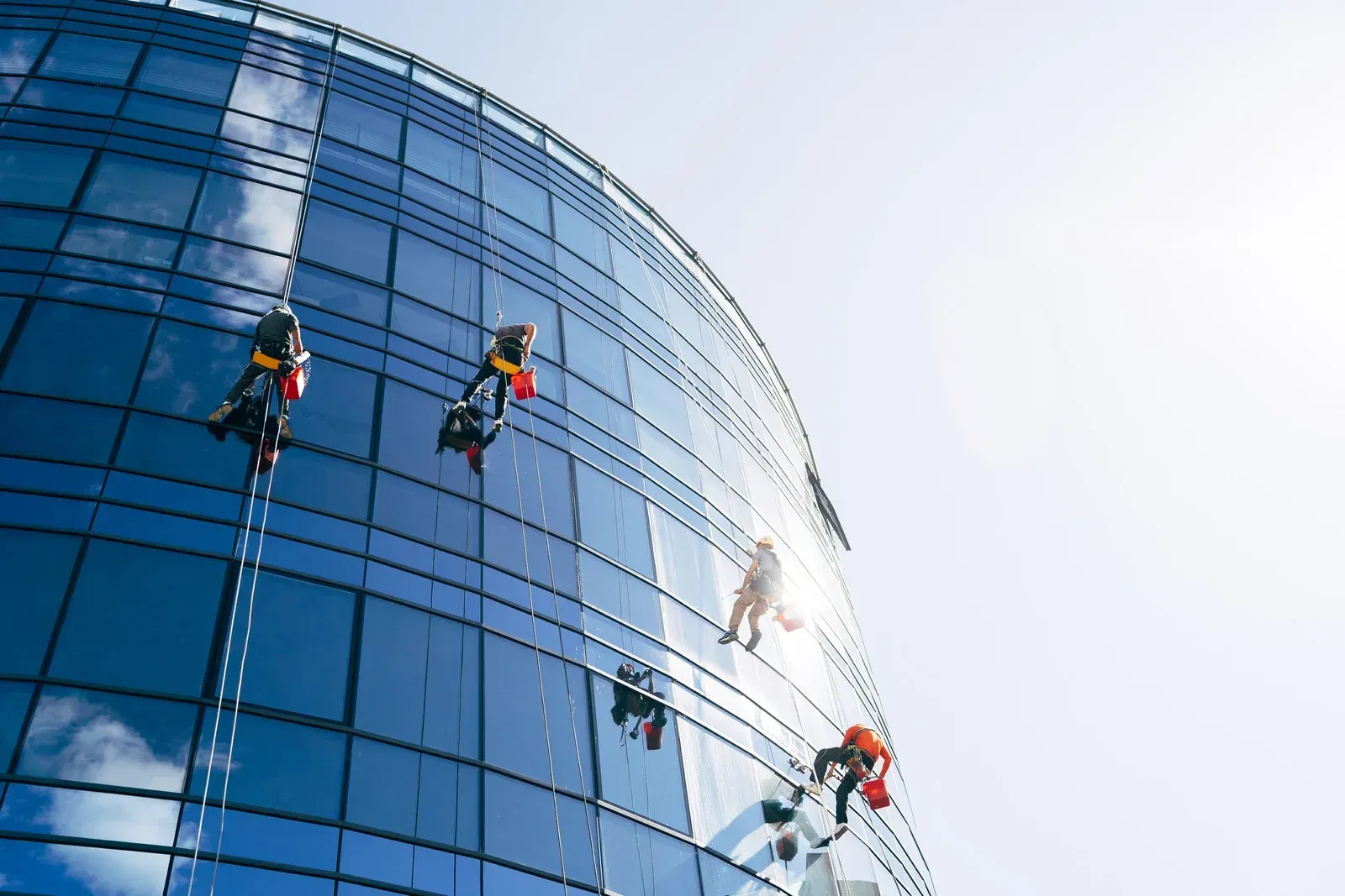 Window washers on a tall, modern building, suspended in the air.