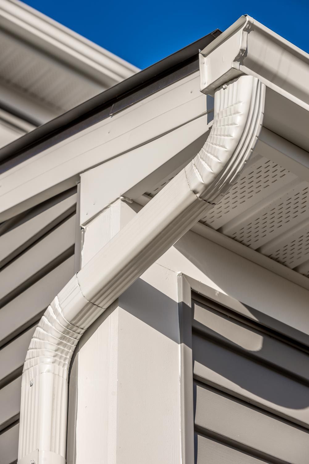 White rain gutter and downspout on a house roof corner against blue sky