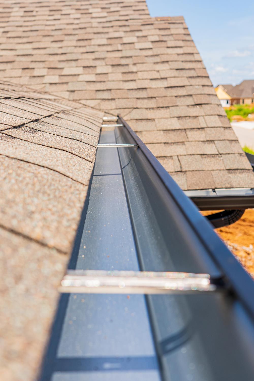 Gutter installed along shingled roof eave, showing close-up of black metal channel.