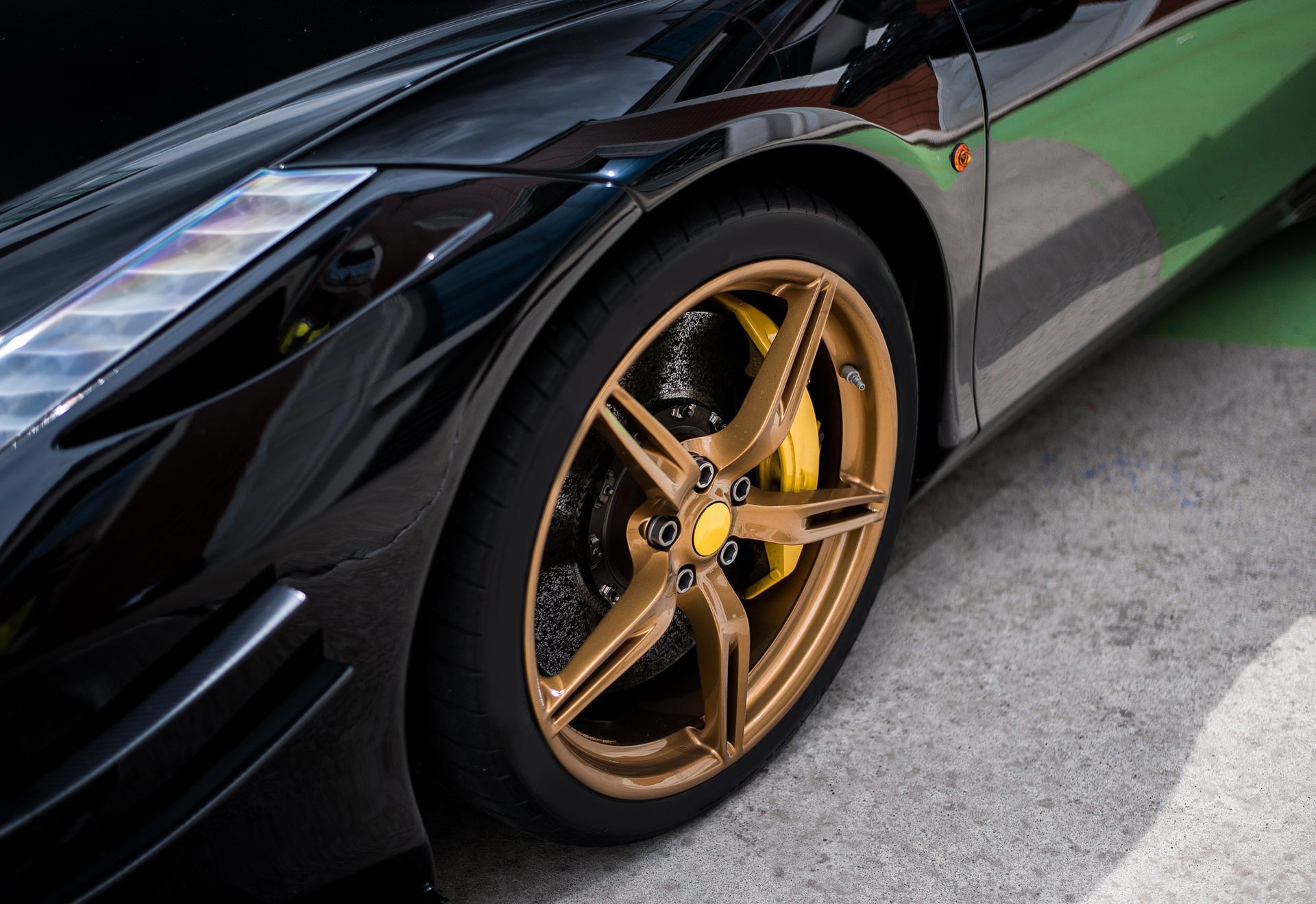 Black sports car with gold rims and yellow brake calipers parked on concrete.