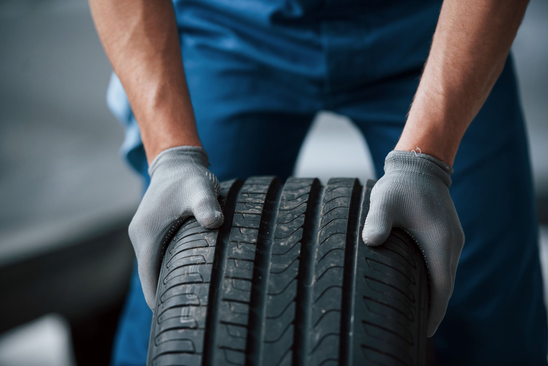 Person in blue jumpsuit and gloves holding a tire.