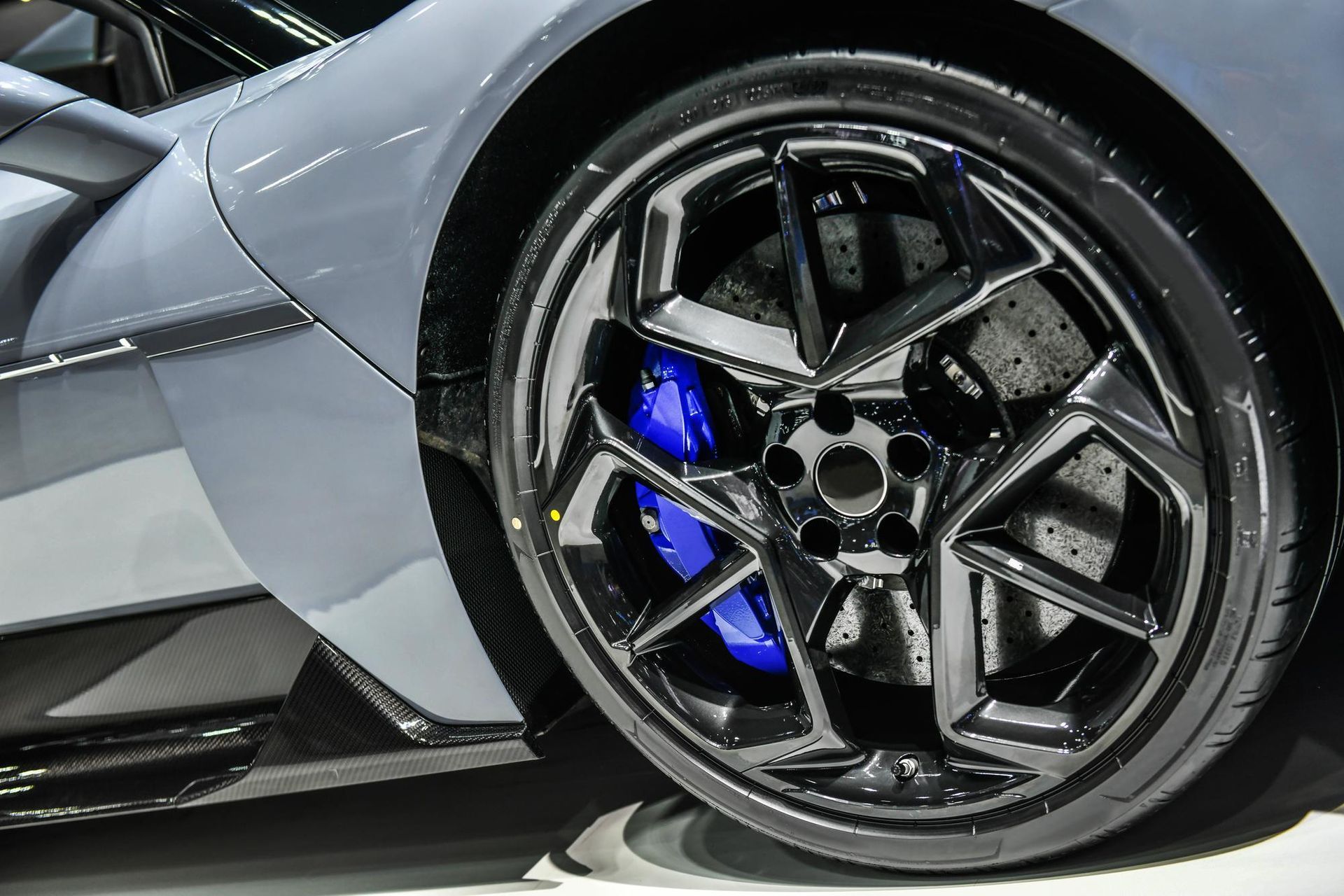 Close-up of a grey sports car wheel with a glossy black rim and blue brake calipers.