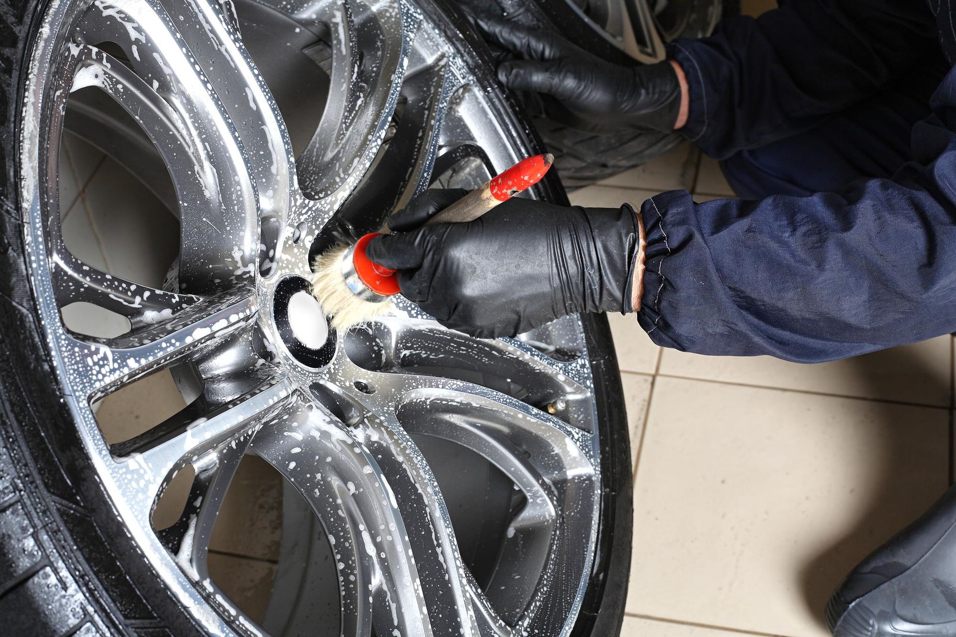 Person wearing black gloves cleaning a car rim with a brush.