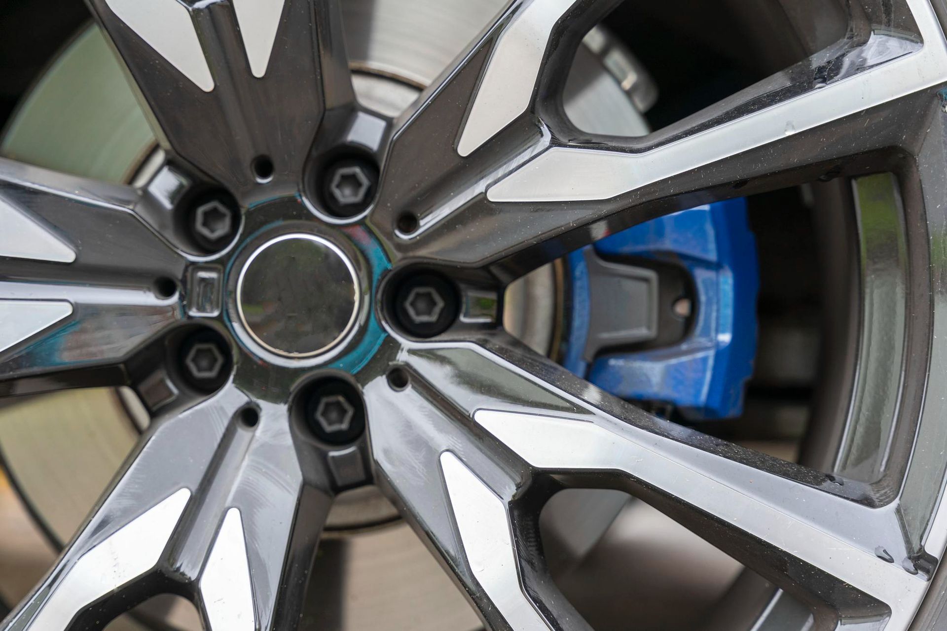Close-up of a car wheel with a silver and black rim, and a blue brake caliper.