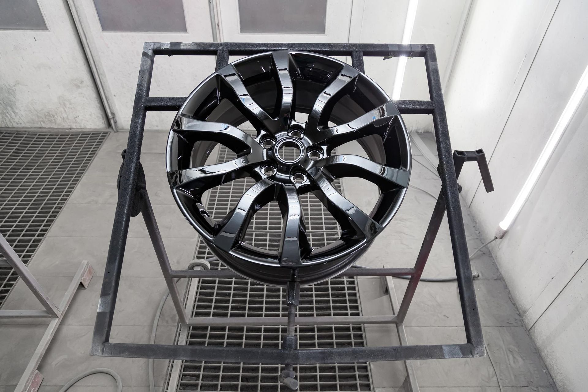 Black car wheel suspended on a frame in a spray paint booth.