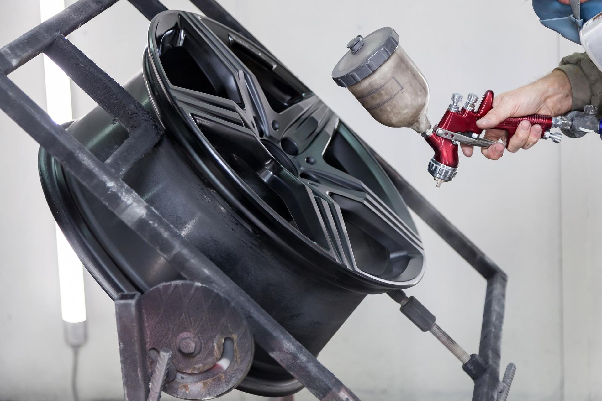 Person spray-painting a black car wheel with a paint gun in a workshop setting.