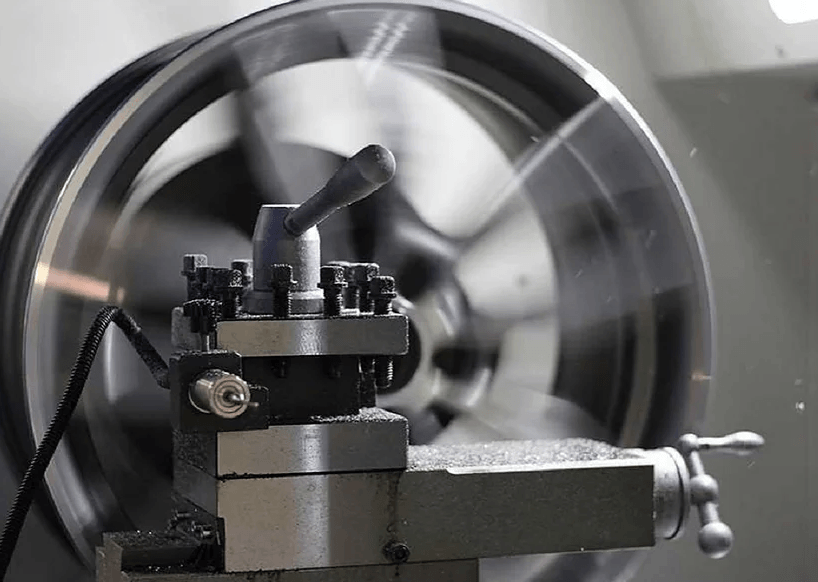 Lathe machining a metal piece; spinning wheel with cutting tool, indoor industrial setting.