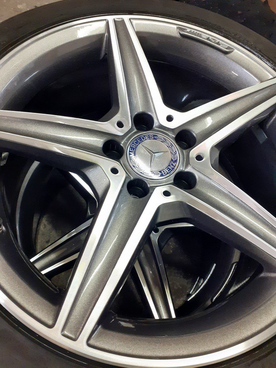 Silver and grey Mercedes-Benz five-spoke alloy wheel with a blue logo in the center.
