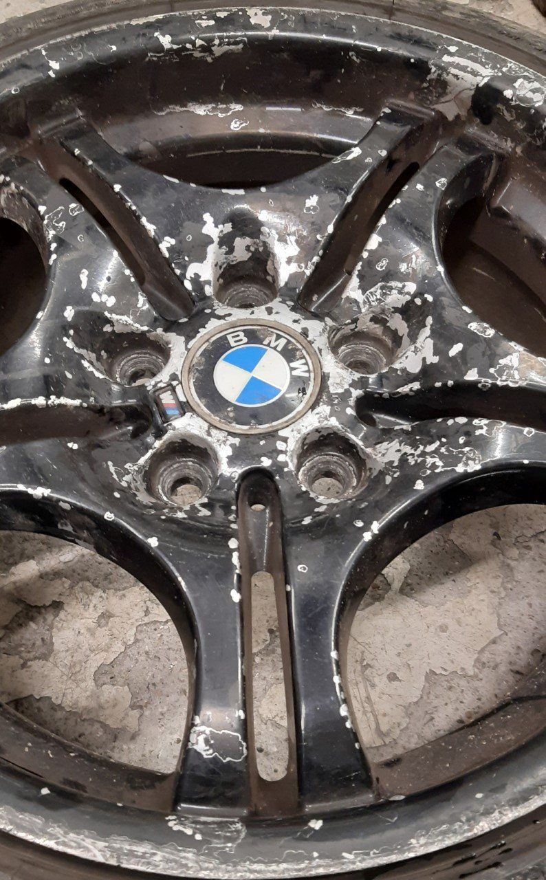 Black BMW car wheel with peeling paint and BMW logo.