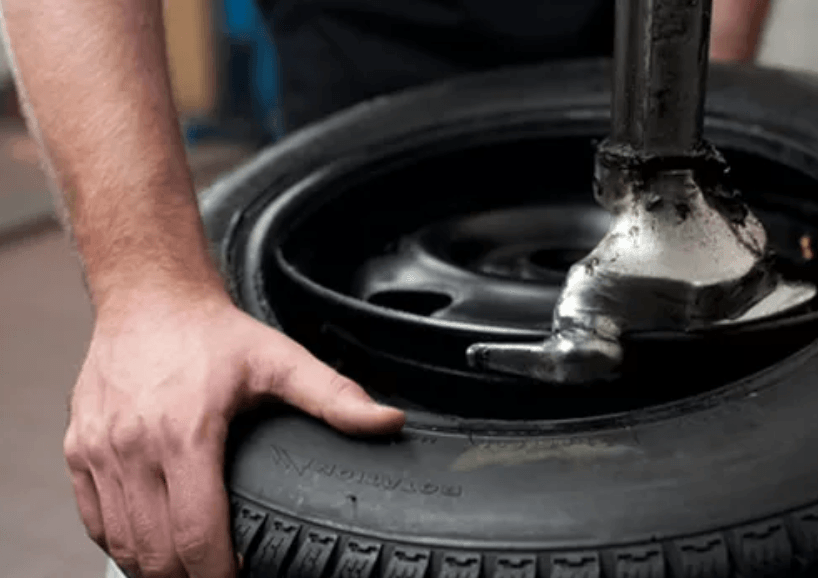 Man using a tire machine to remove a tire from a black rim.
