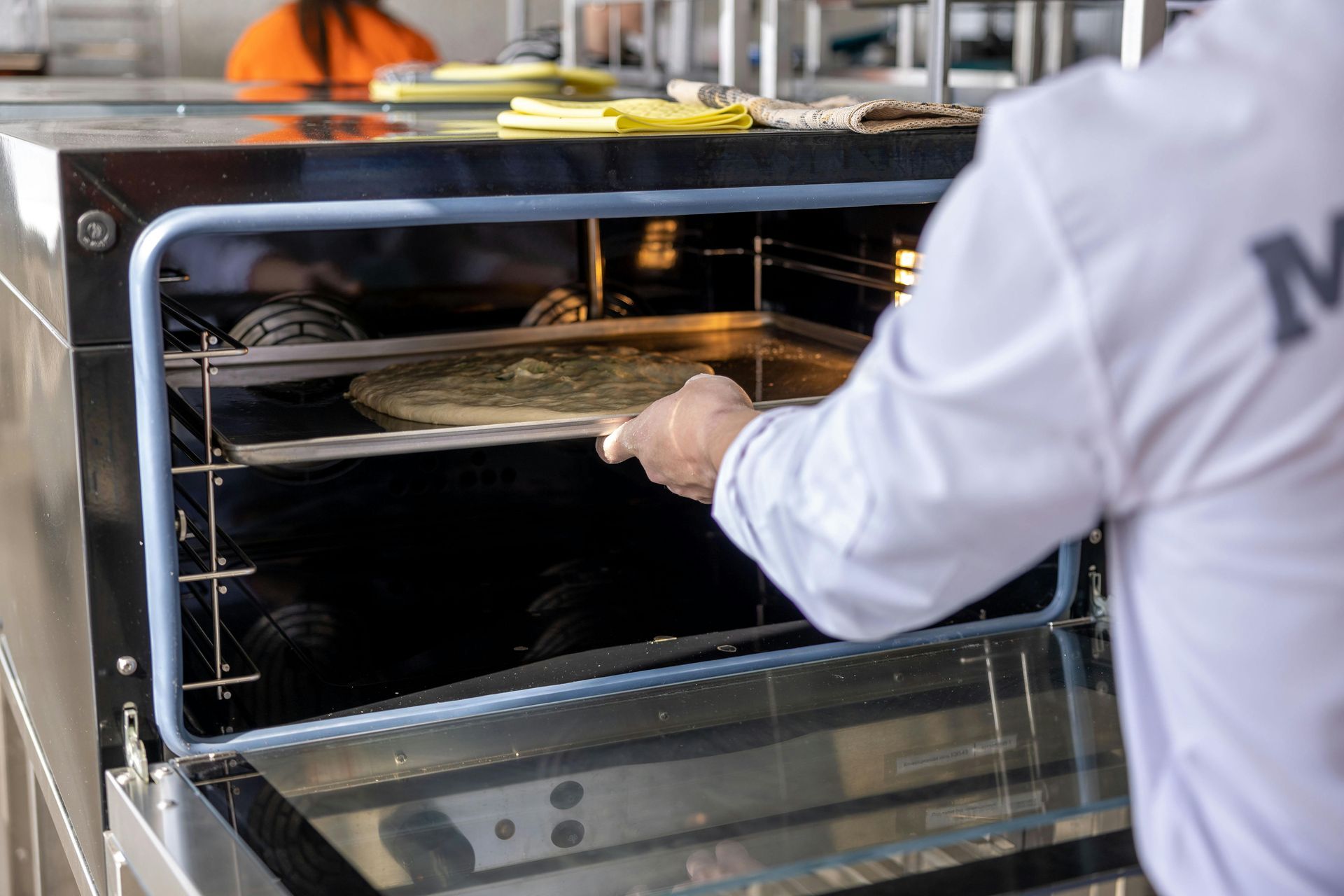 Person loading a tray into a commercial oven in a kitchen