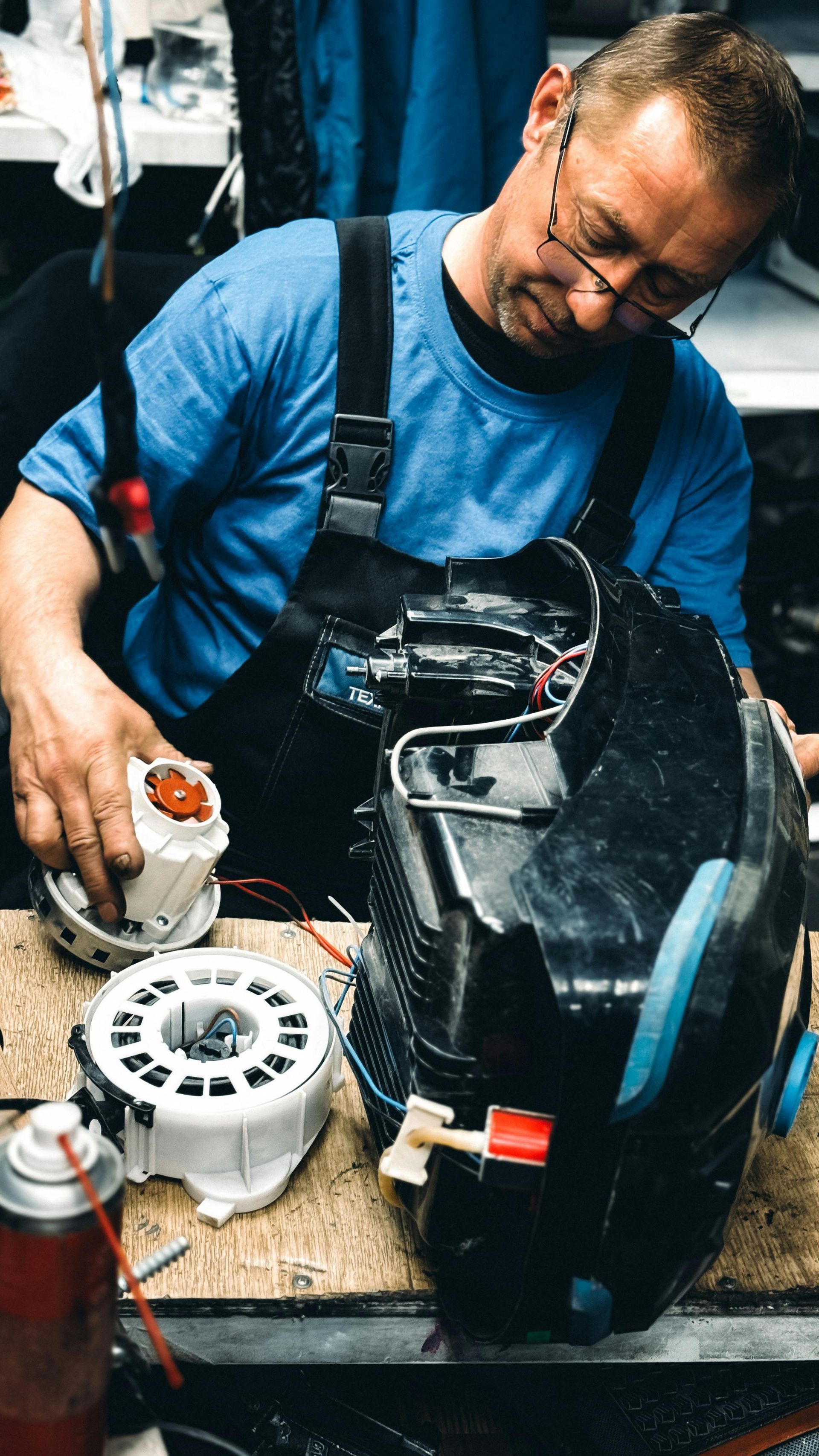 Mechanic in blue shirt working on a black vehicle part with tools in a workshop