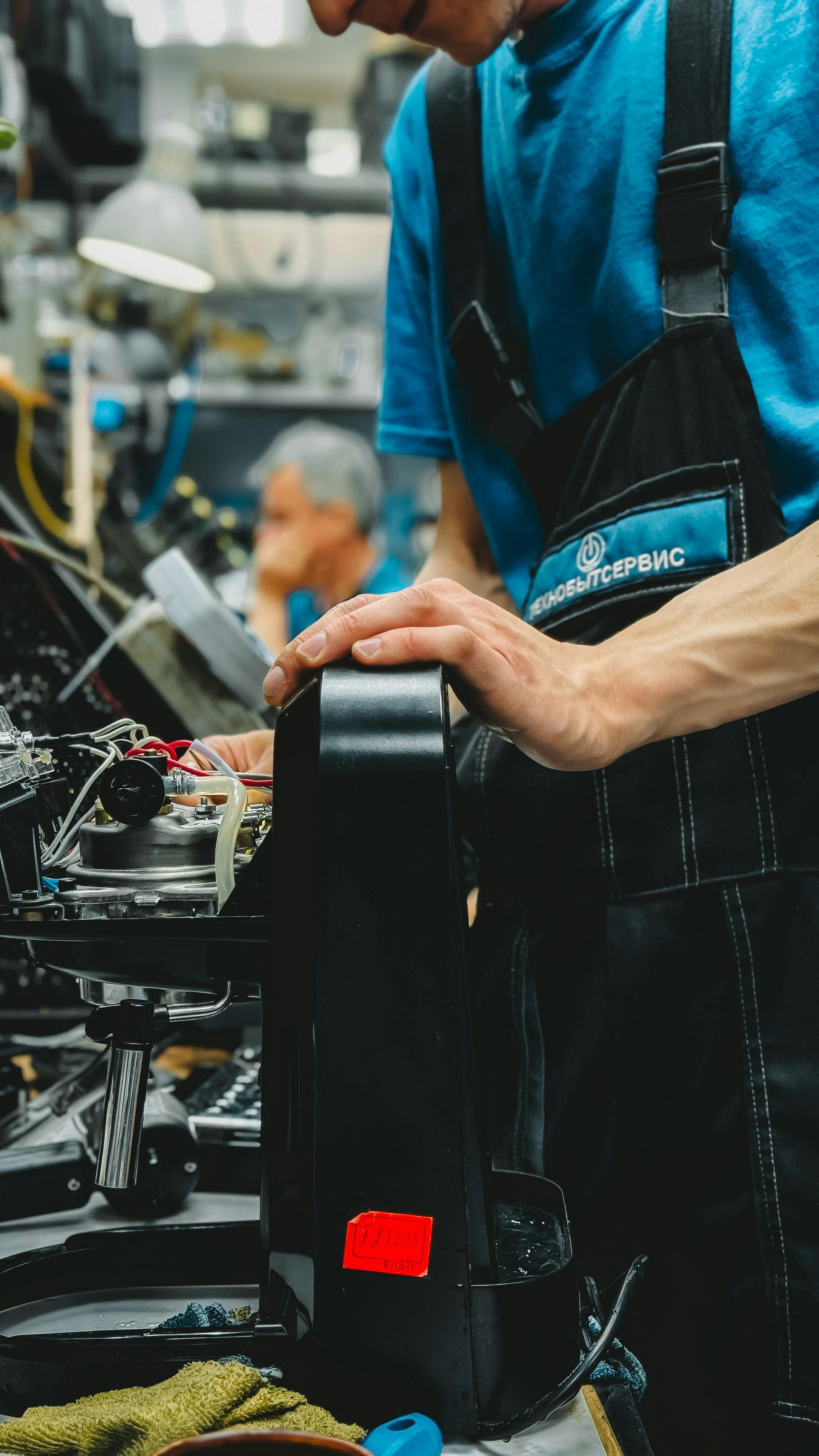 Factory worker handling a black automotive part on an assembly line, with machinery in the background
