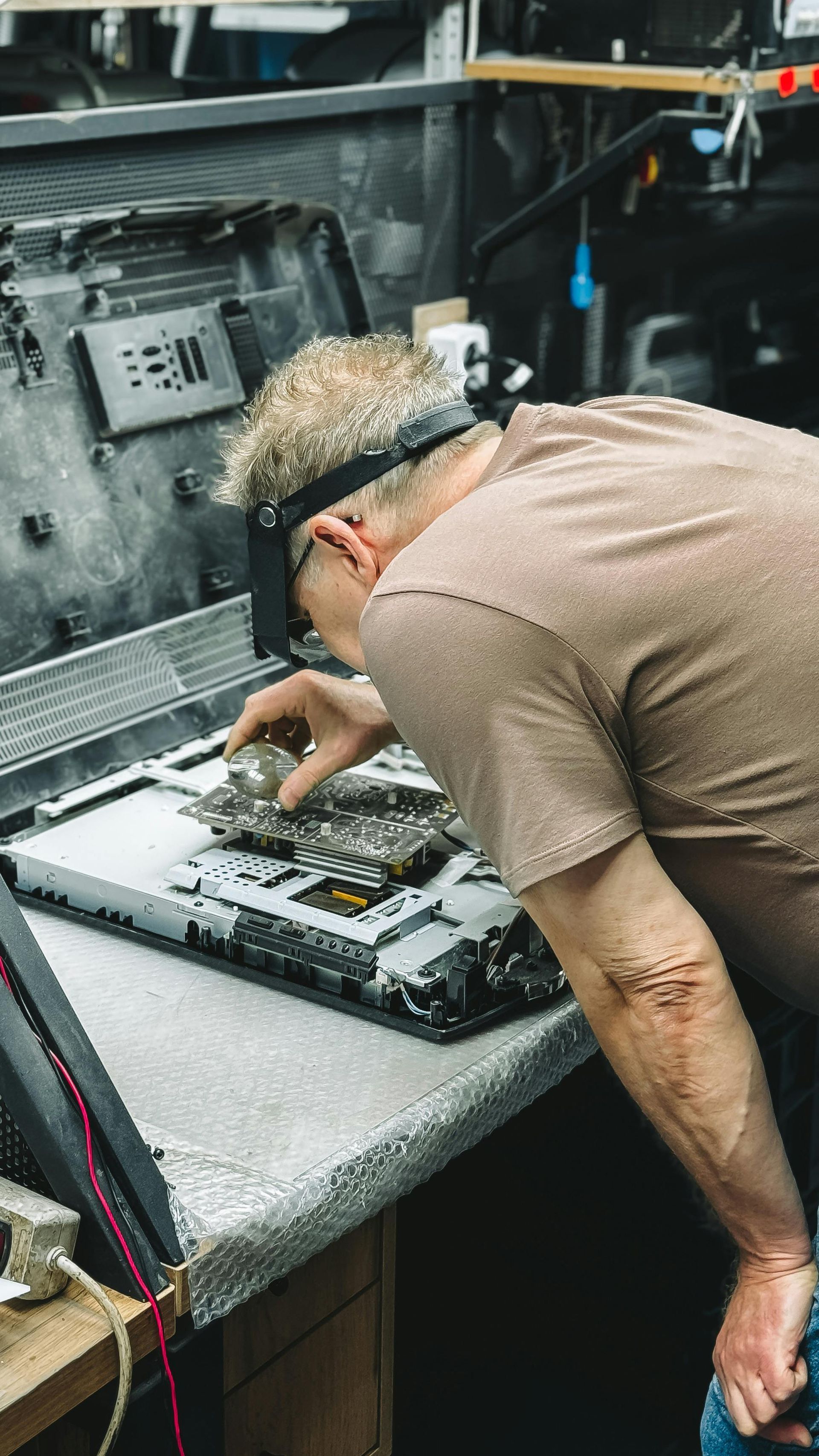 Technician working inside an open laptop on a repair bench with tools and parts nearby