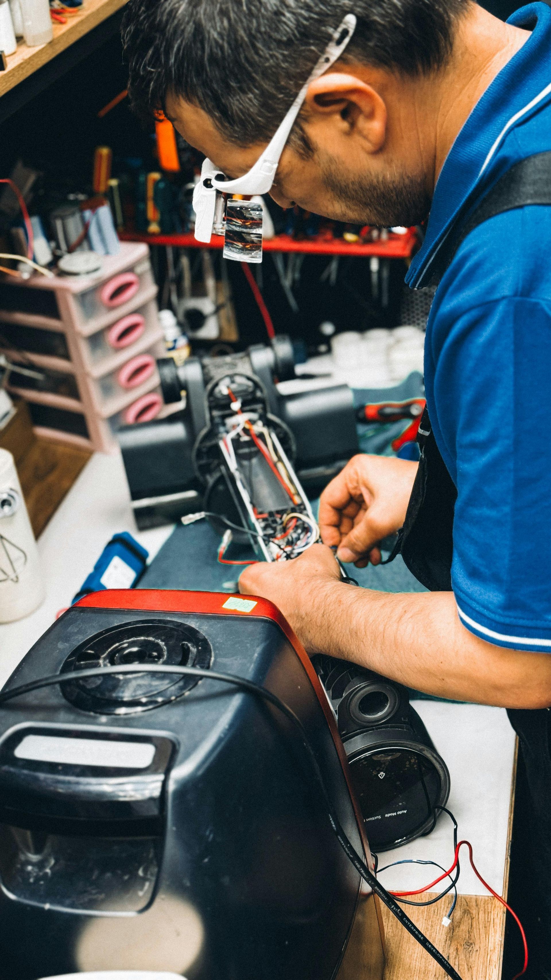 Person repairing a black speaker with tools in a cluttered workshop