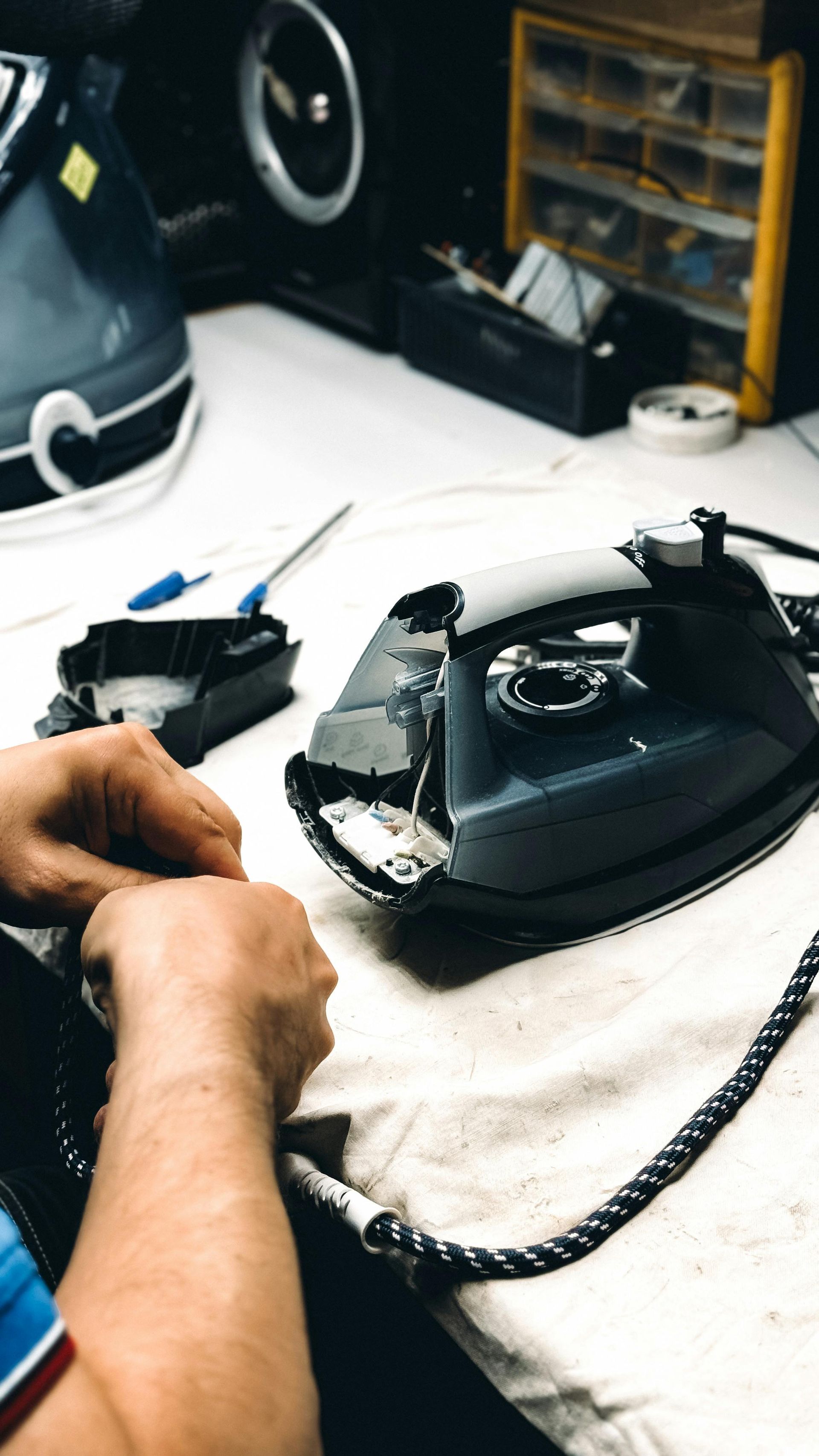 Hands repairing a black appliance on a workbench with tools nearby