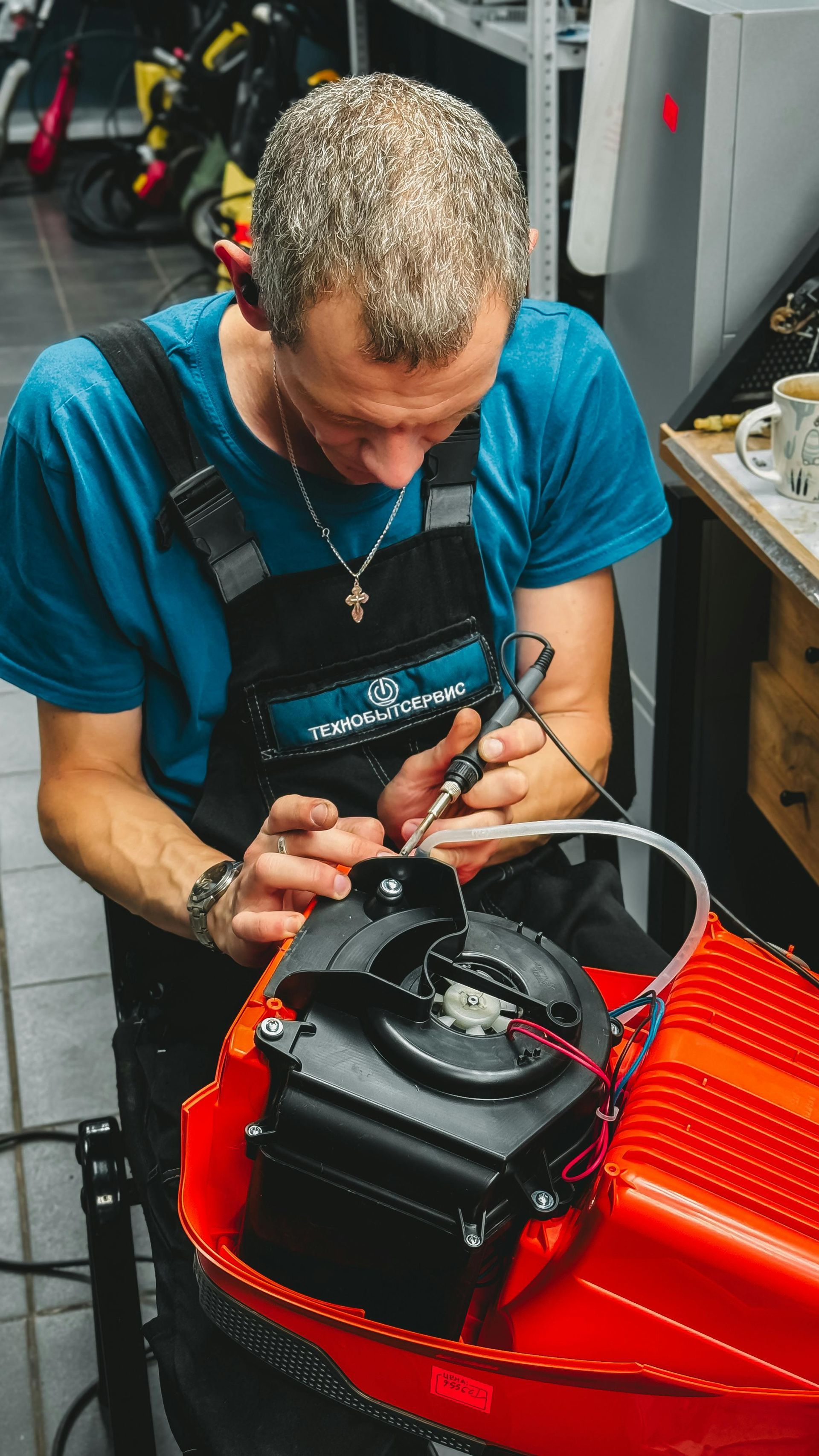 Technician in blue shirt repairing a black device on a red workbench in a workshop