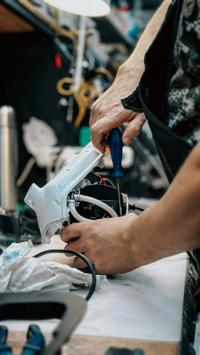 Hands using a white hot glue gun to assemble a small wired device on a workbench