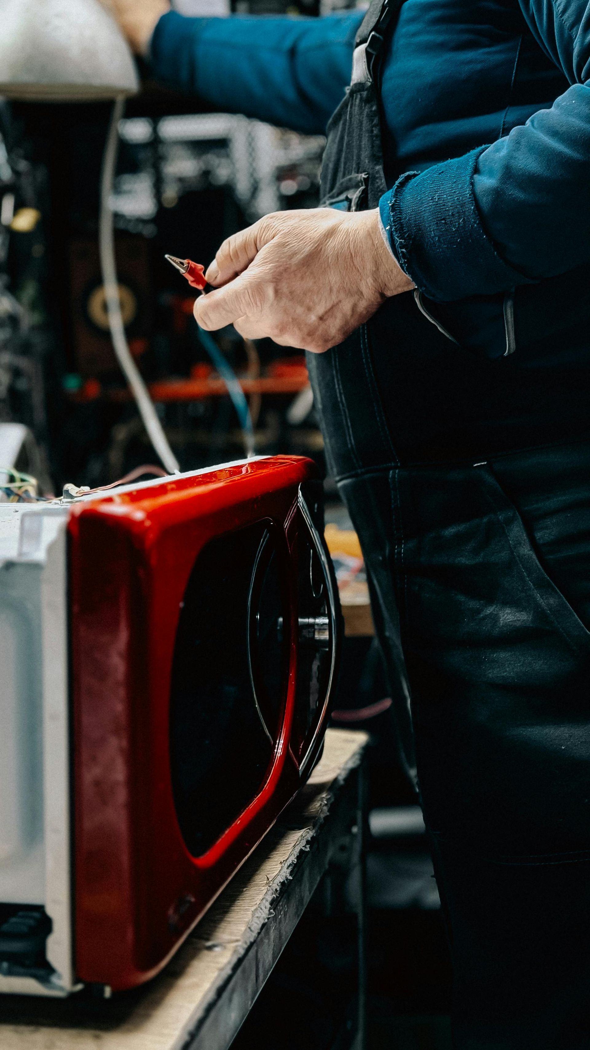 Hands using a tool to repair a red appliance on a workbench