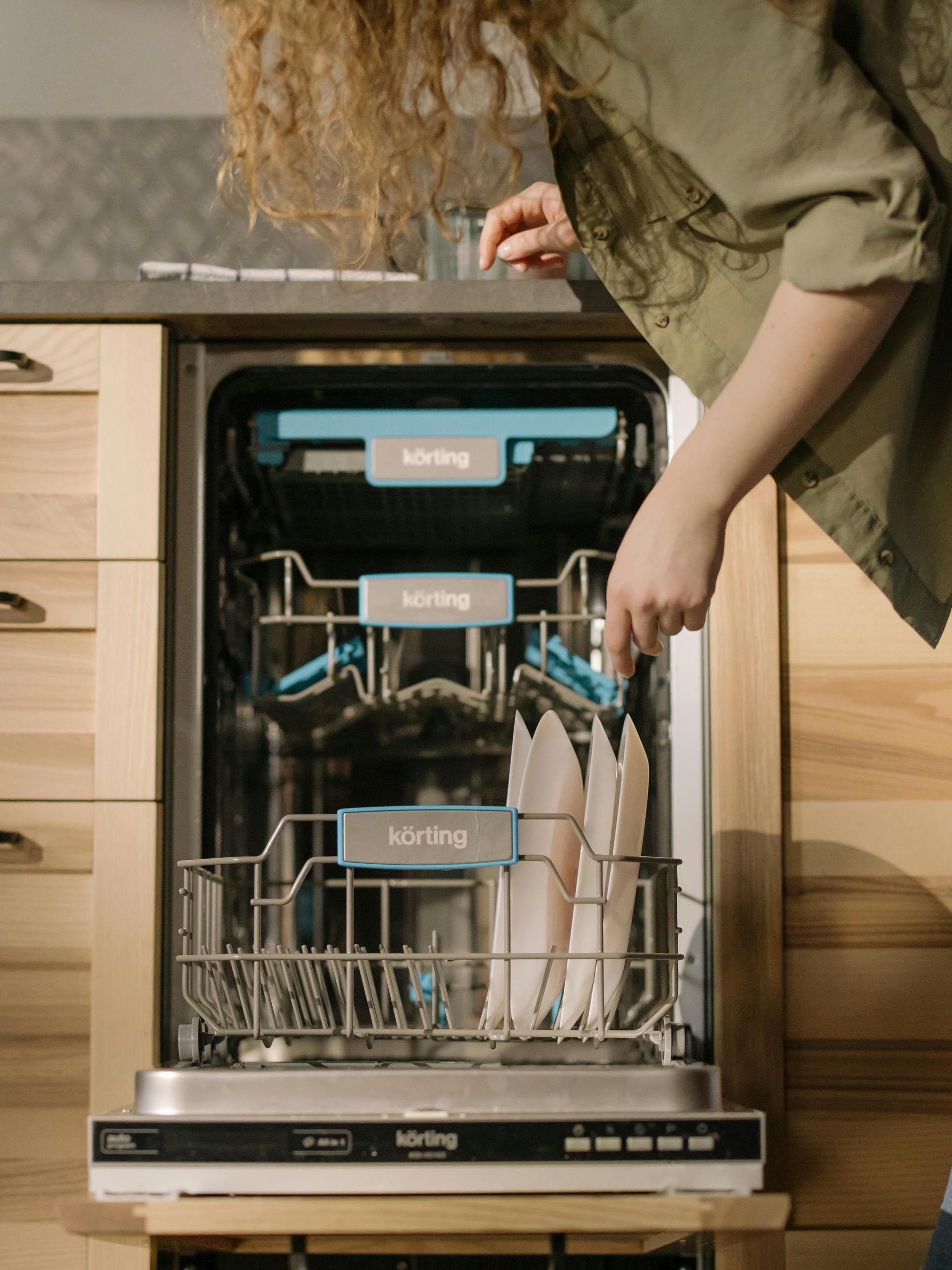 Person loading dishes into an open built-in dishwasher in a kitchen