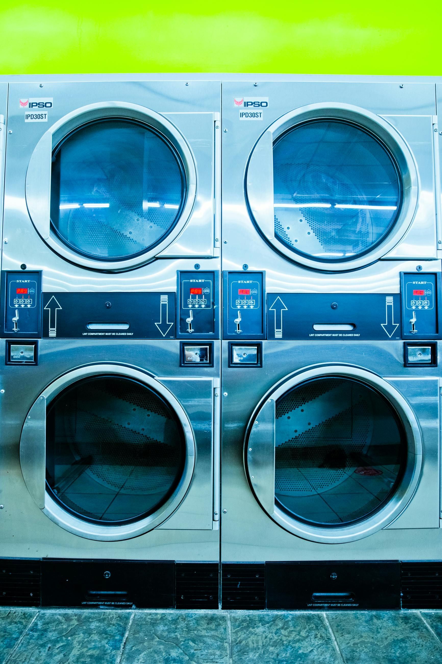 Stacked coin-operated laundry dryers with blue doors in a laundromat.