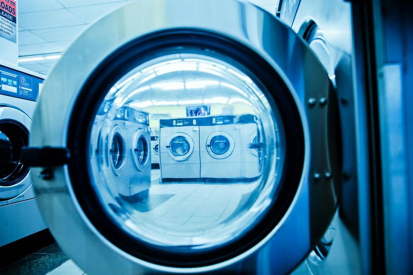 Laundry machines seen through a round washing machine door in a blue-lit laundromat