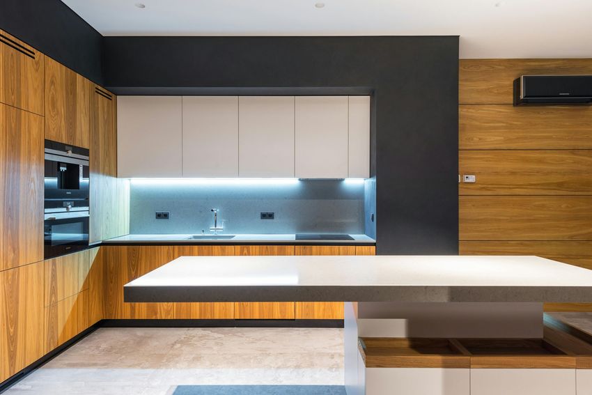 Modern minimalist kitchen with wood cabinets, white island, and backlit backsplash cabinets