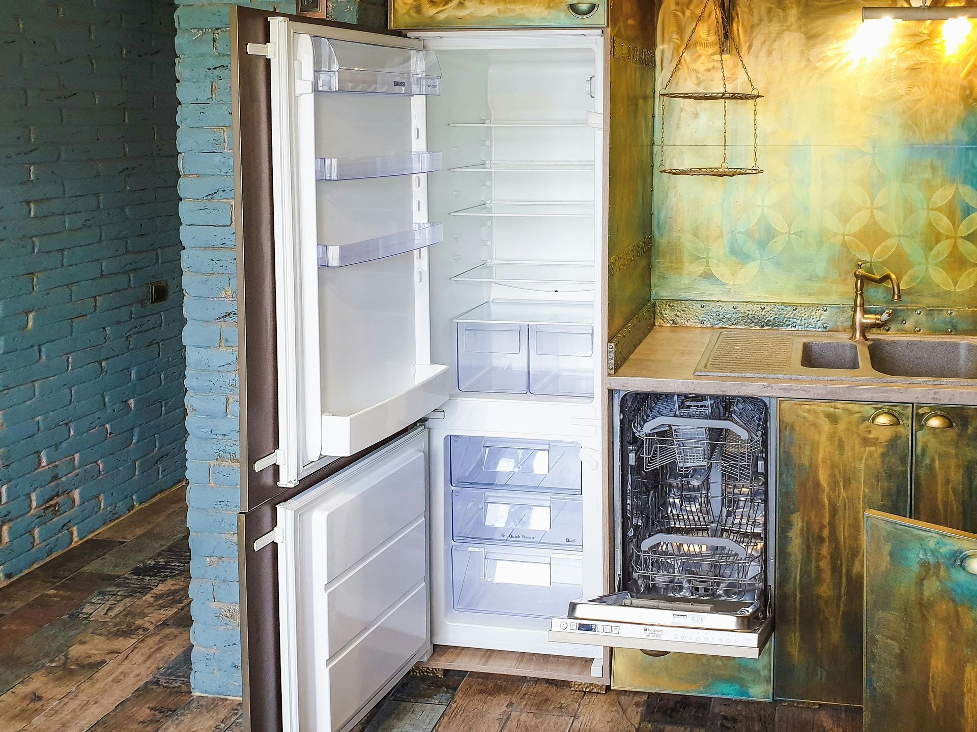 Open refrigerator beside a worn kitchen counter in a dim room with teal brick walls.